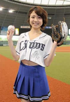 Woman in a baseball uniform and pleated skirt holding a baseball and glove on a field