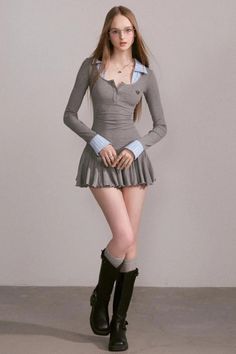 Woman with long hair and glasses wearing a gray dress and black boots