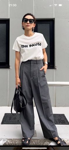 Woman in sunglasses, white t-shirt, and wide leg pants holding a black handbag