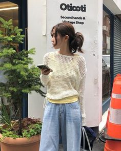 Woman in a loose knit sweater and wide leg jeans holding a phone on a street