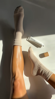 Legs with one sock on, a lotion tube, and strong sunlight shadows