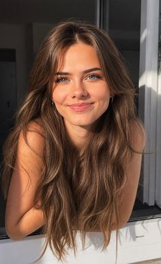 Young woman with long brown hair and blue eyes smiling in natural light