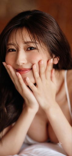 Woman with long hair smiling and holding her face, showing cleavage
