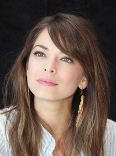 Woman with long brown hair and green eyes wearing gold earrings
