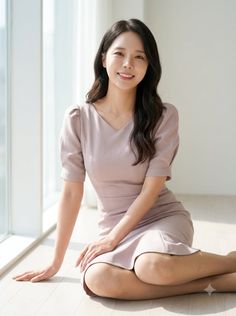 Woman with long dark hair in a light pink dress sitting on the floor indoors