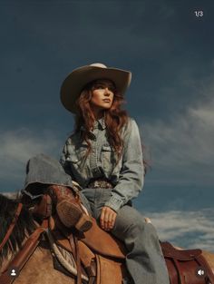 Woman in a cowboy hat and denim outfit riding a horse under a dramatic sky
