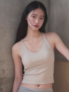 Woman with long black hair wearing a crop top and underwear, leaning against a wall