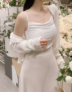 Woman in a white top and long skirt with a cardigan, surrounded by flowers