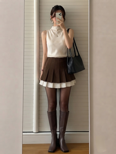 Woman in a brown pleated skirt and knee-high boots taking a mirror selfie