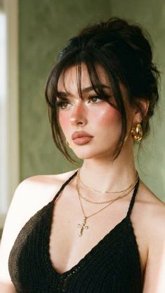 Woman with dark hair and bangs wearing a black top and gold jewelry