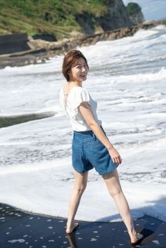 Woman with short hair in denim shorts standing on a beach with ocean waves