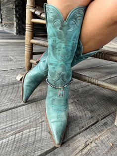 Person wearing turquoise cowboy boots with a boot bracelet on a wooden floor