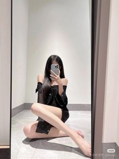 Woman with long black hair taking a mirror selfie while sitting on the floor