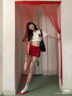 Woman in a red mini skirt and crop top posing with red string curtains
