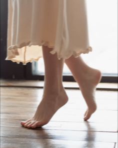 Bare feet and legs of a person in a light-colored dress on a wooden floor