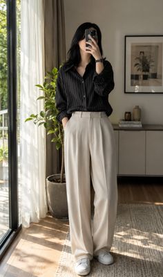 Woman in a striped shirt and wide leg pants taking a mirror selfie indoors