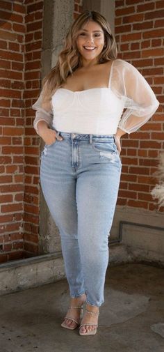 Woman with long hair wearing a white top and light wash jeans, smiling indoors