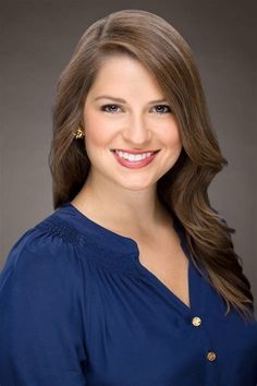 Woman with long brown hair wearing a blue blouse and gold earrings, smiling