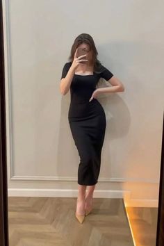 Woman in a black dress and high heels taking a mirror selfie