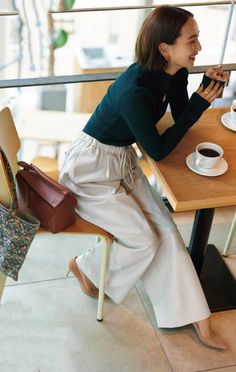 Woman in a green turtleneck and wide leg pants sitting at a coffee shop
