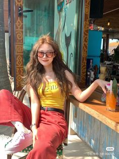 Woman with long wavy hair and sunglasses sitting outdoors with a cocktail