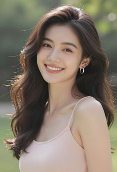 Woman with long wavy hair and hoop earrings smiling in a pink camisole outdoors