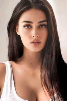 Woman with long dark hair wearing a white tank top, looking directly at the camera