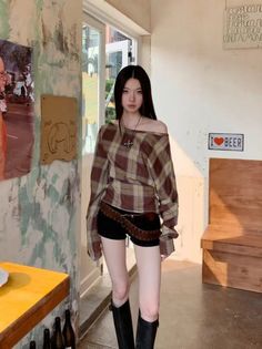 Woman with long black hair wearing a plaid off-shoulder shirt and black shorts indoors