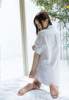 Woman in a white shirt kneeling on a bed by a window