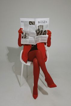 Person in a red outfit and gloves reading a newspaper while sitting on a white chair