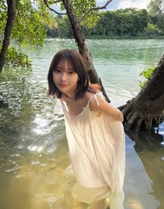 Woman in a white dress standing in water with trees around her