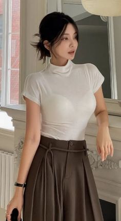 Woman in a white turtleneck and brown pants with an updo hairstyle indoors
