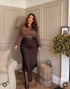 Woman in a brown top and skirt with boots standing in an indoor setting