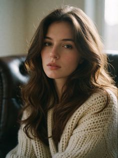 Woman with long brown hair wearing a knitted sweater, lit by soft indoor light