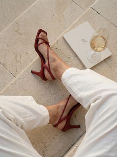 Person wearing red high heels and white pants, relaxing outdoors with a glass of wine