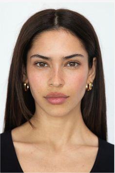 Woman with long dark hair and gold hoop earrings looking directly at the camera