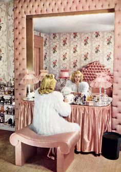 Woman in a white fur coat at a pink vanity table in a vintage bedroom