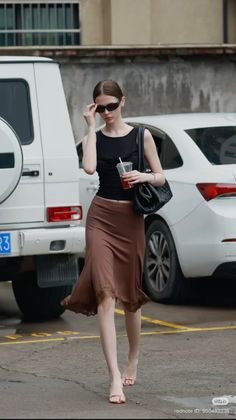 Woman in a black top and brown skirt walking outdoors with sunglasses