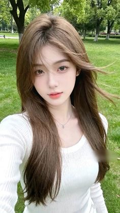 Woman with long brown hair wearing a white top in a park