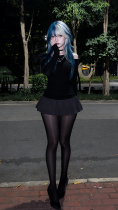 Woman with blue and white hair in a black top and skirt outdoors at night