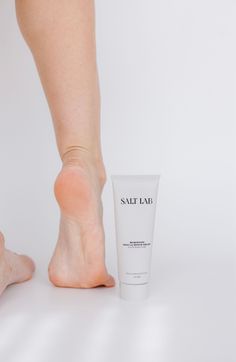 Bare feet next to a white tube of muscle repair cream on a white background