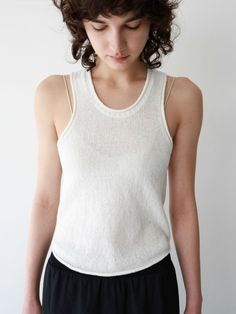 Woman with short curly hair wearing a white tank top and black pants indoors