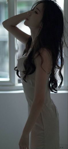 Woman with long dark hair posing by a window in soft lighting