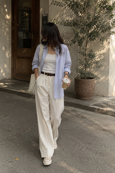 Woman in a striped shirt and wide leg pants walking outdoors with a coffee cup