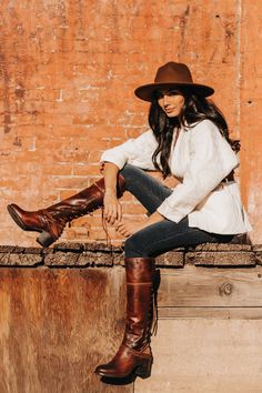 Woman in a brown hat and boots sitting against a brick wall