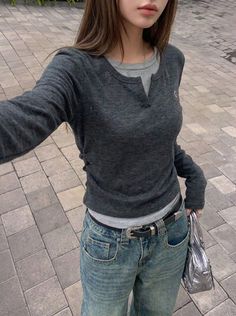 Person in a dark grey long sleeve shirt and blue jeans holding a silver handbag