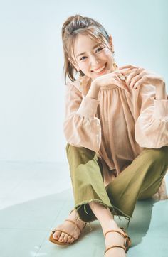 Woman with a ponytail wearing a blouse and cropped pants, sitting on the floor