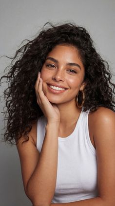 Woman with curly hair and freckles smiling in a white tank top