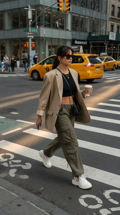 Woman in a crop top, blazer, and cargo pants crossing a city street