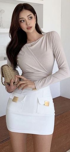 Woman with long dark hair wearing a white skirt and long sleeve top, holding a quilted bag